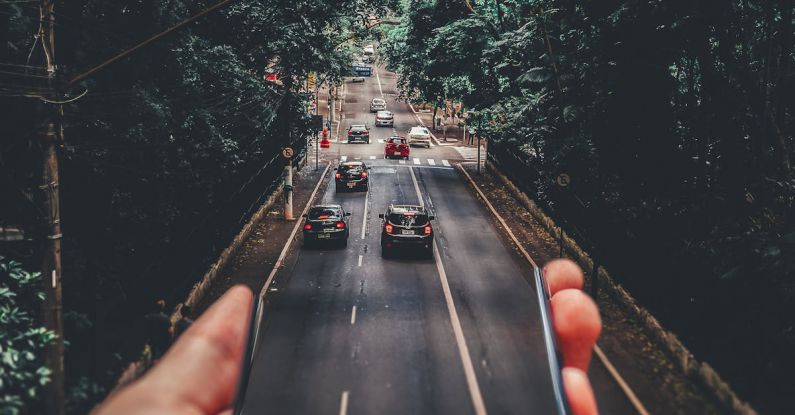 System - Forced Perspective Photography of Cars Running on Road Below Smartphone