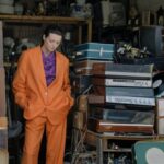 Turntables - A Woman in Orange Suit Standing in a Store with Stacks of Turntables