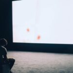 Projector - Man Sitting in Front of Turned-on Screen