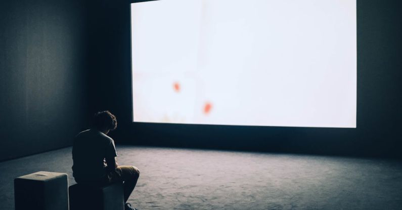 Projector - Man Sitting in Front of Turned-on Screen